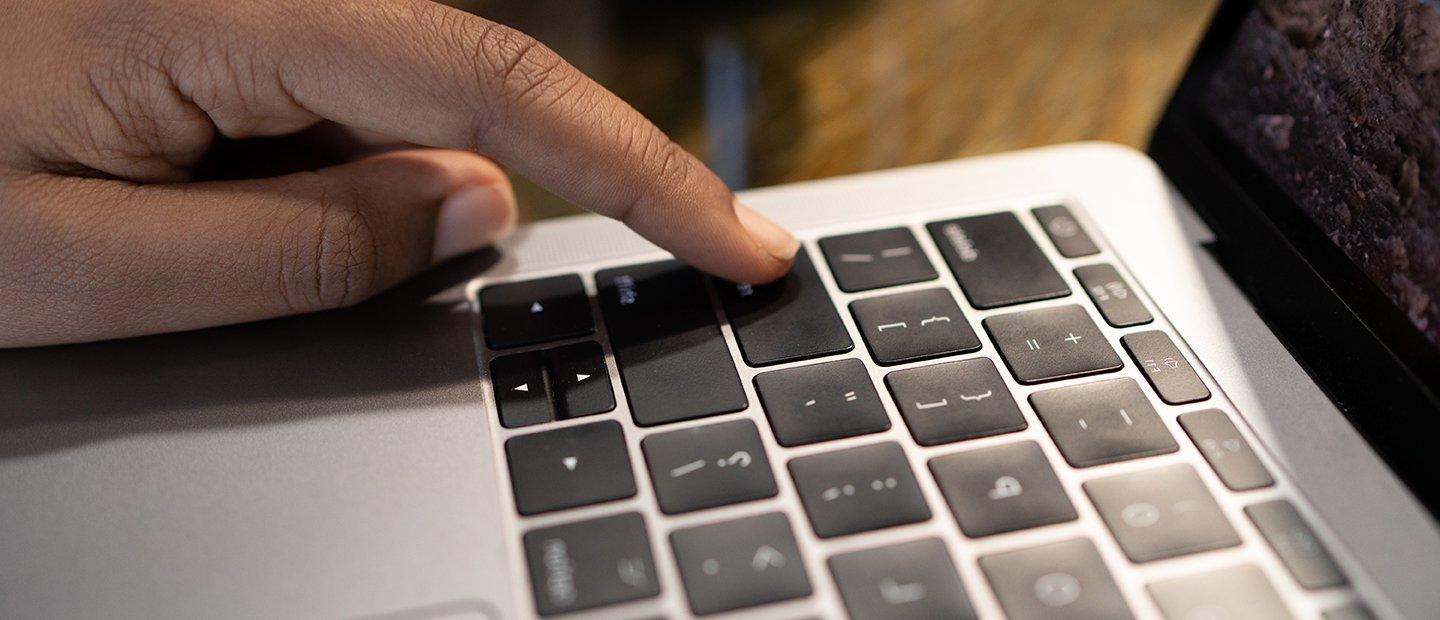 A finger pressing the "enter" key on a laptop.